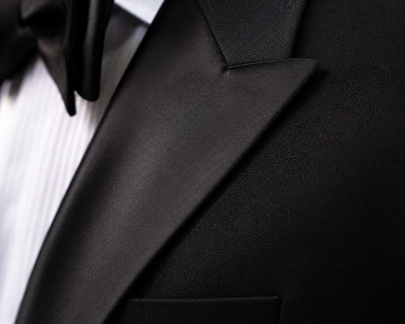 Close-up of a black satin tuxedo lapel and formal shirt details.