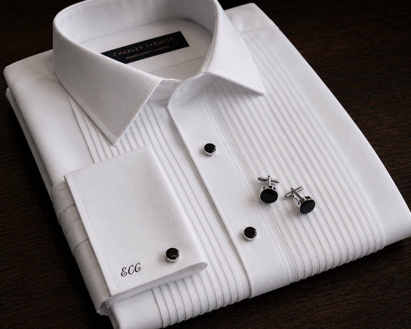 Folded white tuxedo shirt with black studs, cufflinks and monogrammed cuff detail.